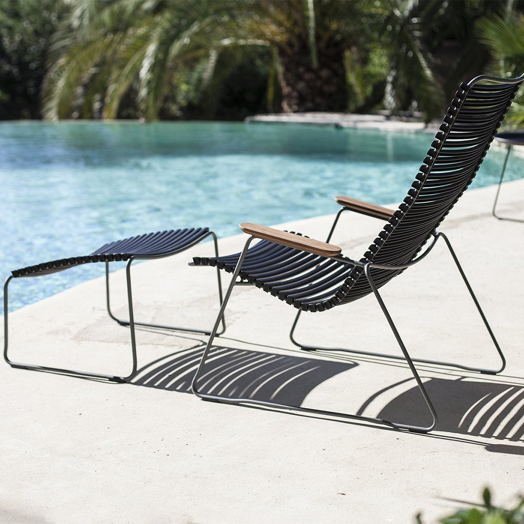 Black slatted lounge chair and ottoman with wooden accents beside a pool, featuring sleek, modern design.