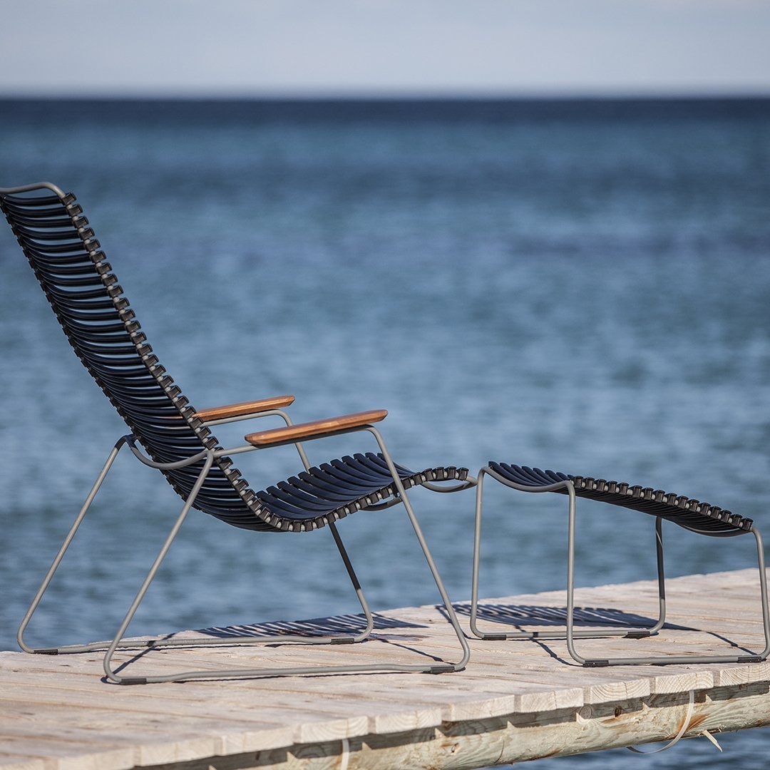 Black and grey striped lounge chair with wooden armrests, set against a serene blue ocean backdrop.