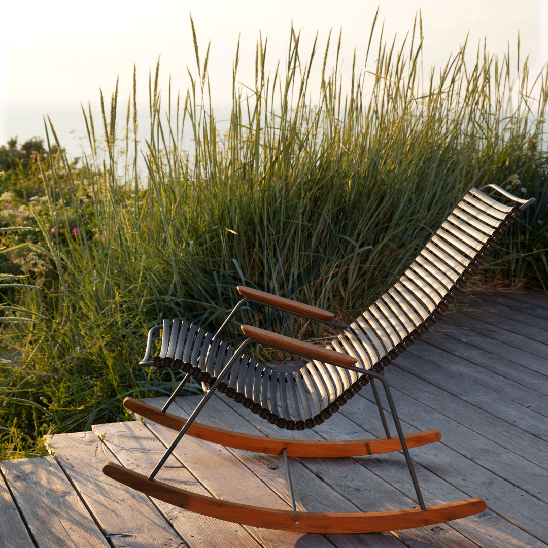Black and white striped rocking chair with wooden armrests, set against lush green grass and a serene backdrop.