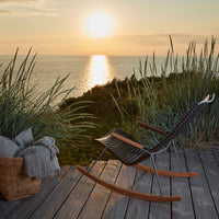 Modern black rocking chair with natural wood accents, set against a sunset backdrop and lush greenery.
