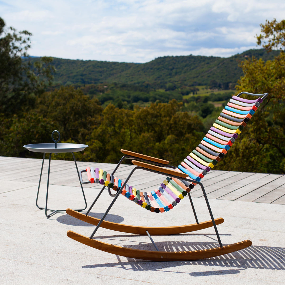 Colorful striped rocking chair with vibrant patterns, set against a scenic outdoor backdrop.