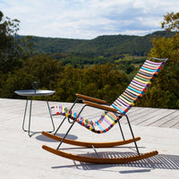 Colorful striped rocking chair with vibrant patterns, set against a scenic outdoor backdrop.
