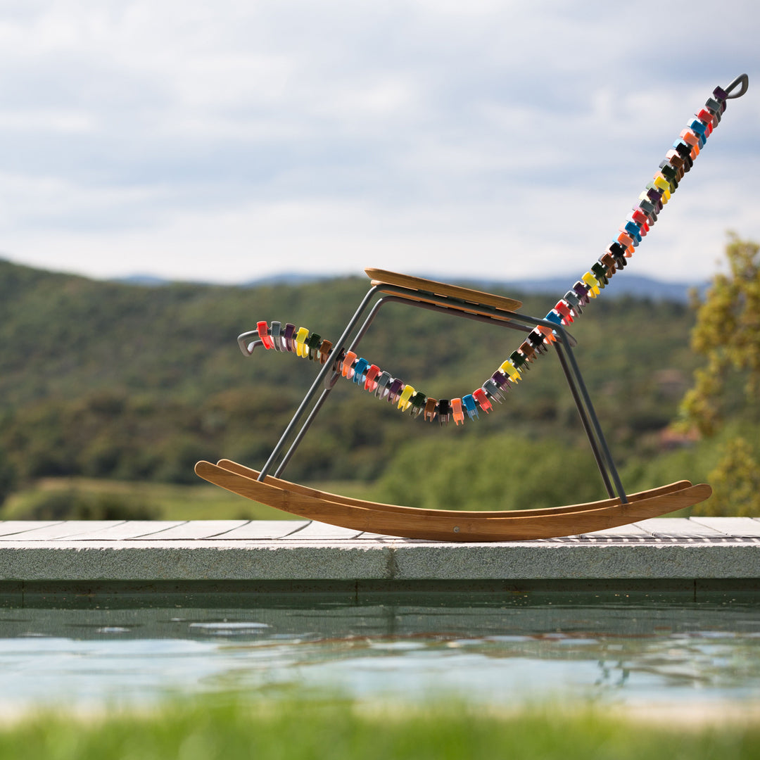 Colorful beaded pattern on a sleek wooden rocking chair with a metallic frame, set against a serene outdoor backdrop.