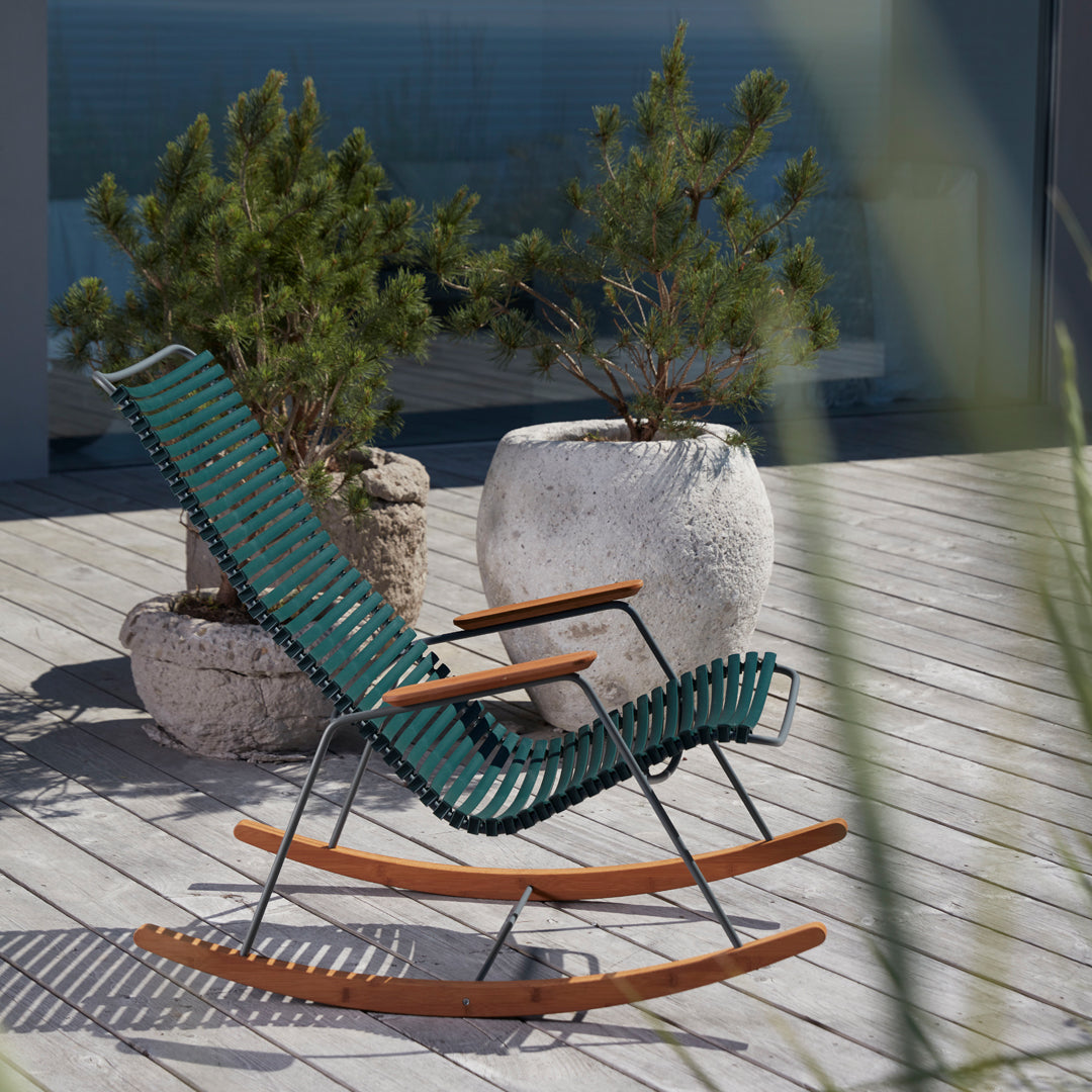 Green and black striped rocking chair with natural wood accents, situated in a modern outdoor setting.