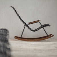 Black spiral accents on a sleek wooden rocking chair against a neutral backdrop, showcasing modern design.