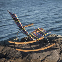 Vibrant striped rocking chair with multicolored fabric against a serene water backdrop. Perfect for outdoor relaxation.
