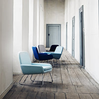 Stylish chairs in light blue, dark blue, gray, and black, set against a minimalist hallway with wooden floors.
