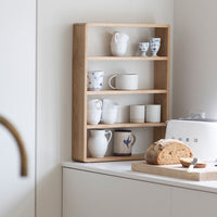 "Wooden shelf displaying white and blue patterned mugs, cream and speckled ceramic cups."