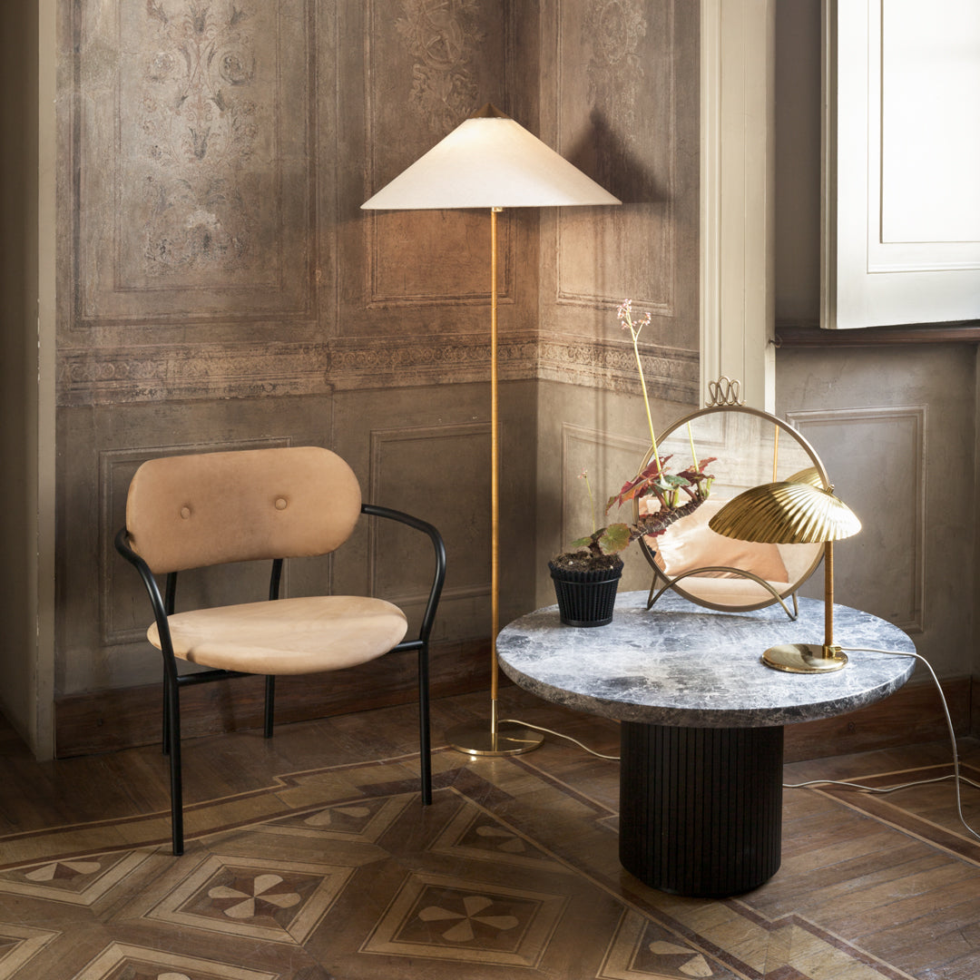 Peach chair with black frame, marble table, gold lamp, and soft lighting against a textured beige wall.