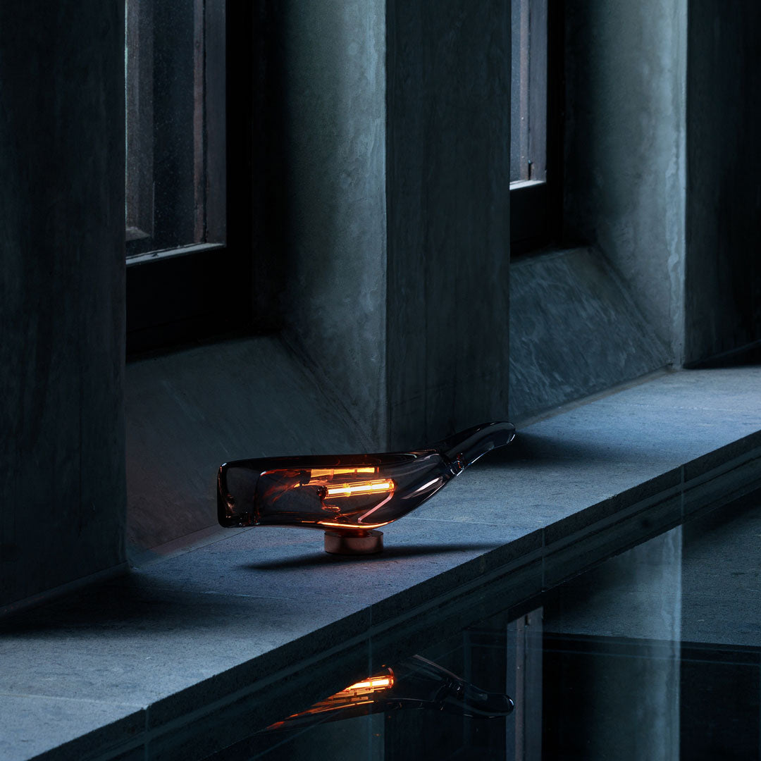 Elegant amber glass lamp with sleek black and gray accents, reflecting softly on a stone surface.
