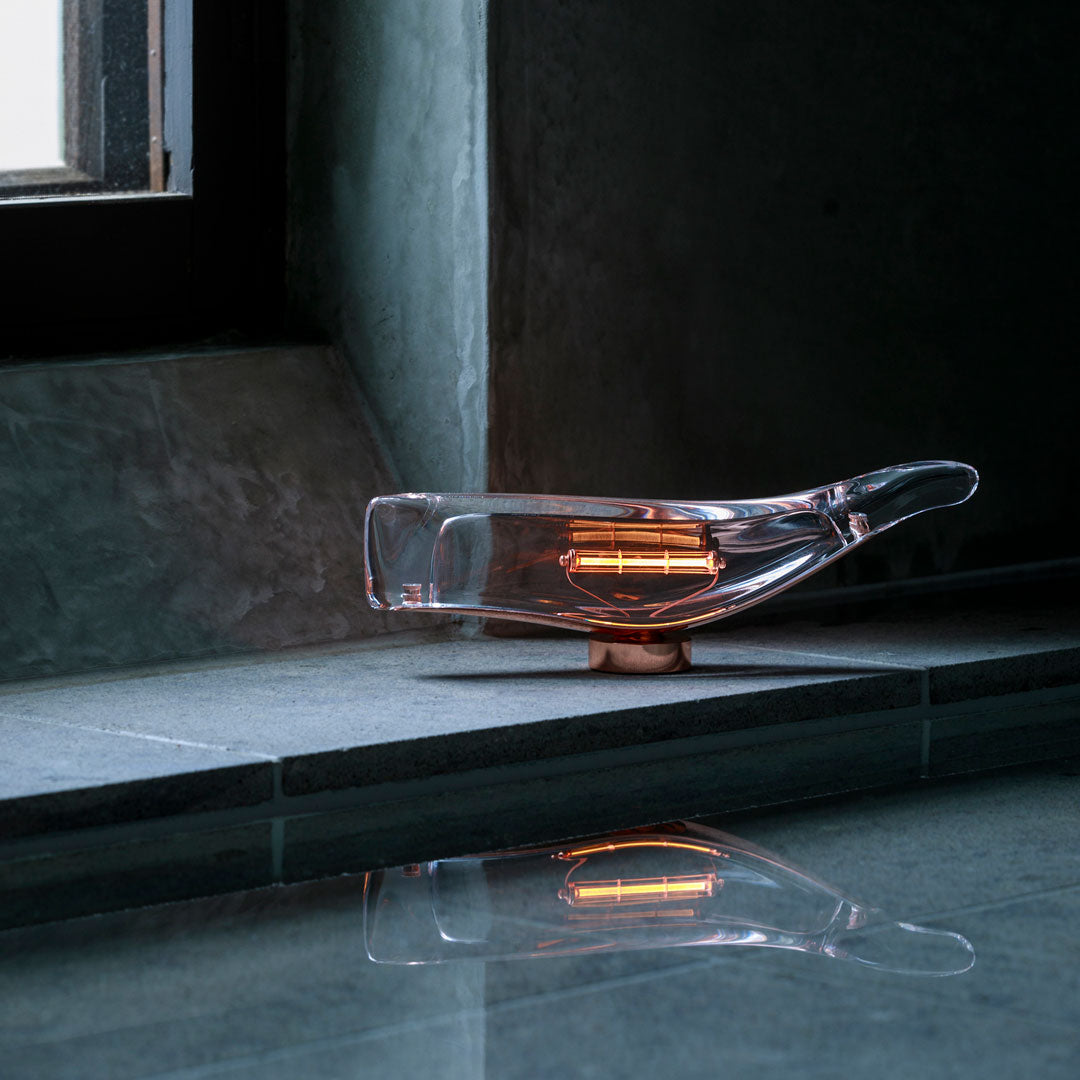 Clear glass lamp with warm amber accents, featuring sleek, modern design on a gray stone surface.
