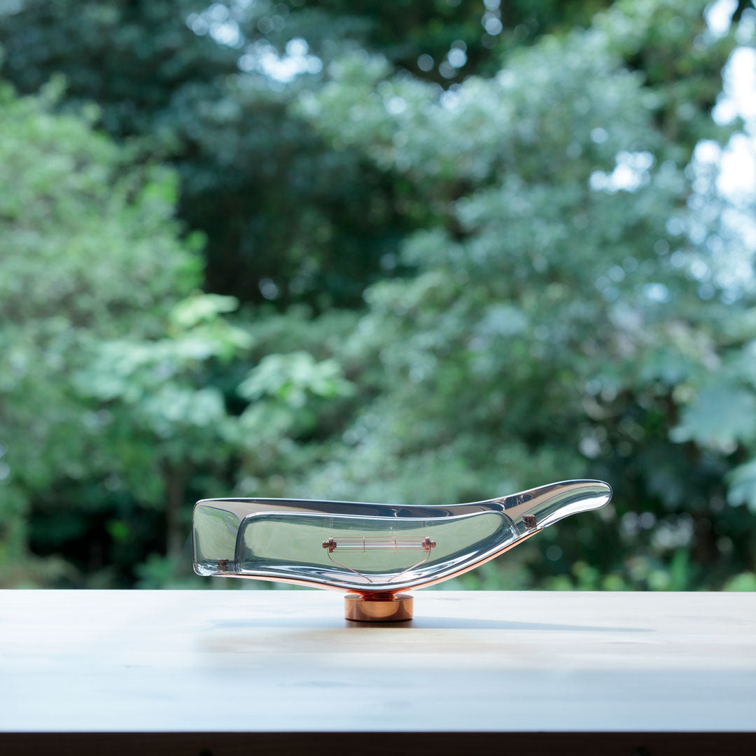 Clear glass bowl with a sleek design, featuring a rose gold base against a soft green outdoor backdrop.