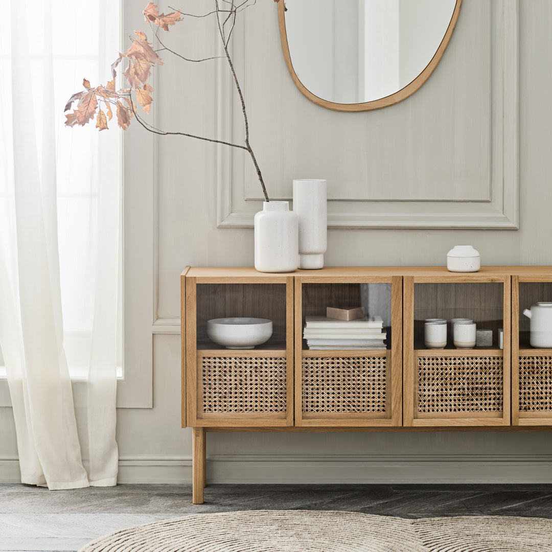 Natural wood sideboard with woven rattan accents, white ceramic decor, and soft neutral tones in a bright, airy setting.