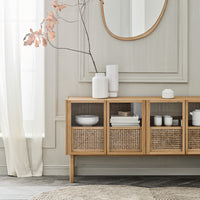 Natural wood sideboard with woven rattan accents, white ceramic decor, and soft neutral tones in a bright, airy setting.