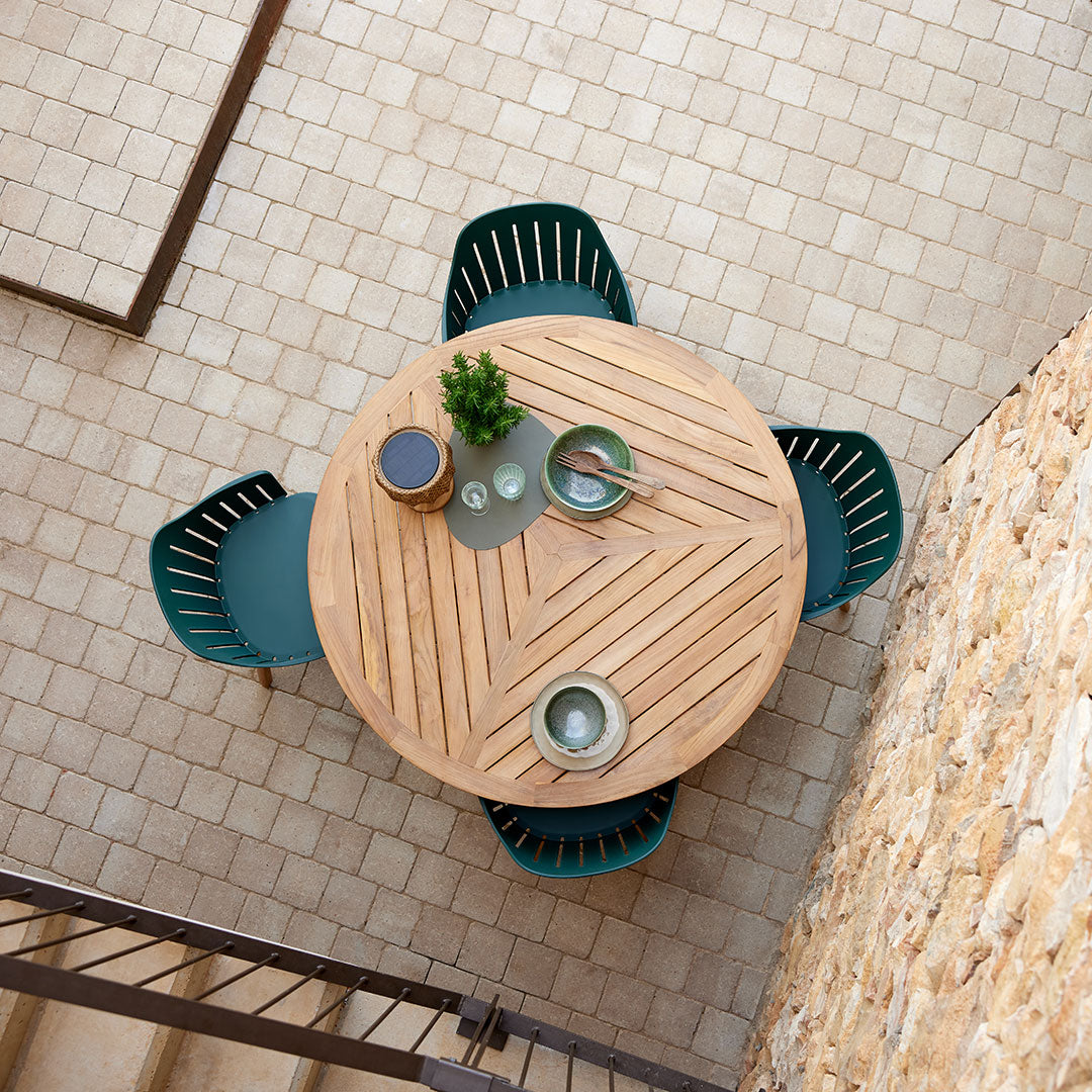 Round wooden table with chevron pattern, surrounded by teal chairs, set on a textured stone floor.