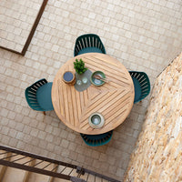 Round wooden table with chevron pattern, surrounded by teal chairs, set on a textured stone floor.