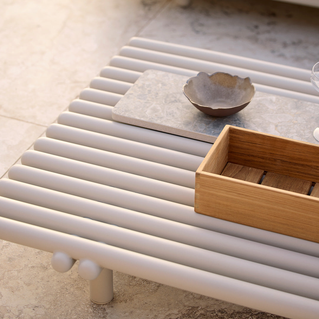 Light gray slatted table with a smooth finish, contrasting wooden tray, and stone-textured accent.