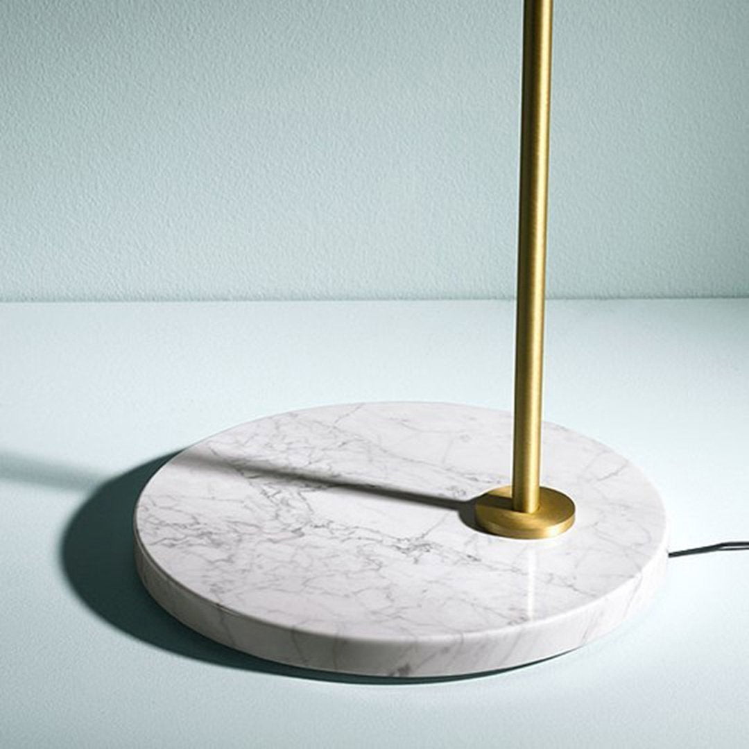 Sleek gold lamp stand with a textured white marble base set against a soft blue background.