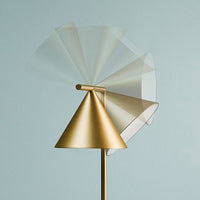Gold modern lamp with a conical base and transparent fan blades, set against a soft blue background.