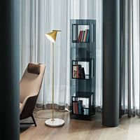 Modern black mesh bookshelf with gold accents, accompanied by a beige chair against a backdrop of gray curtains.