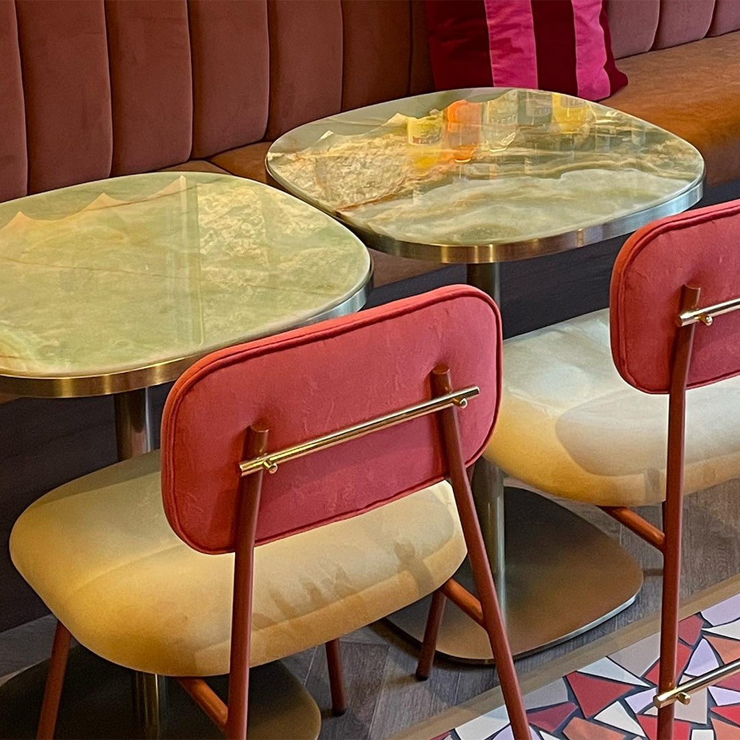 Modern tables with glossy green tops and stylish red and beige chairs against a geometric patterned floor.