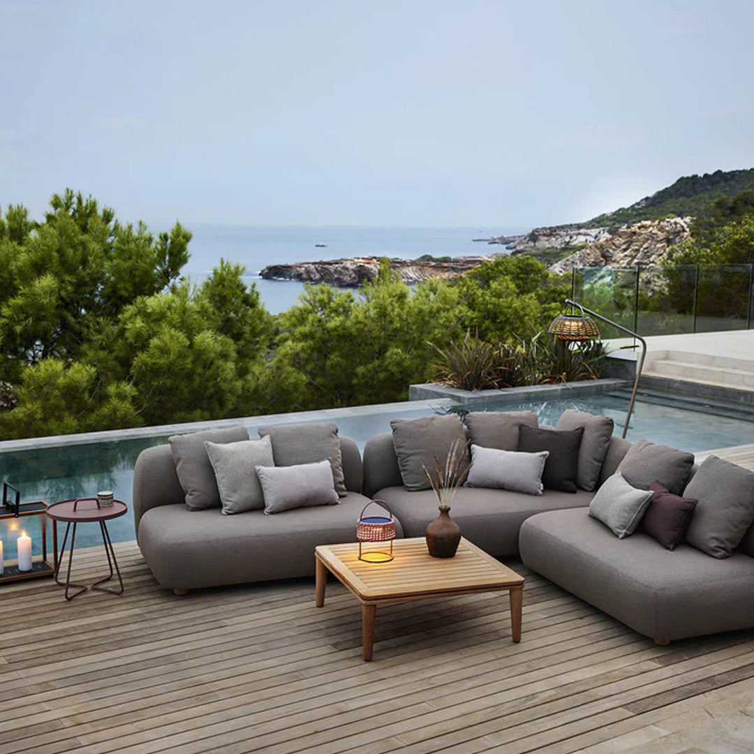 Cozy outdoor lounge set featuring gray cushions, a light wooden table, and subtle earth tones against a serene backdrop.