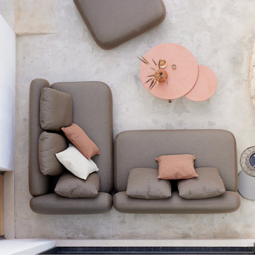Modern brown sectional sofa with soft cushions in cream and terracotta, paired with round pink tables and a neutral floor.