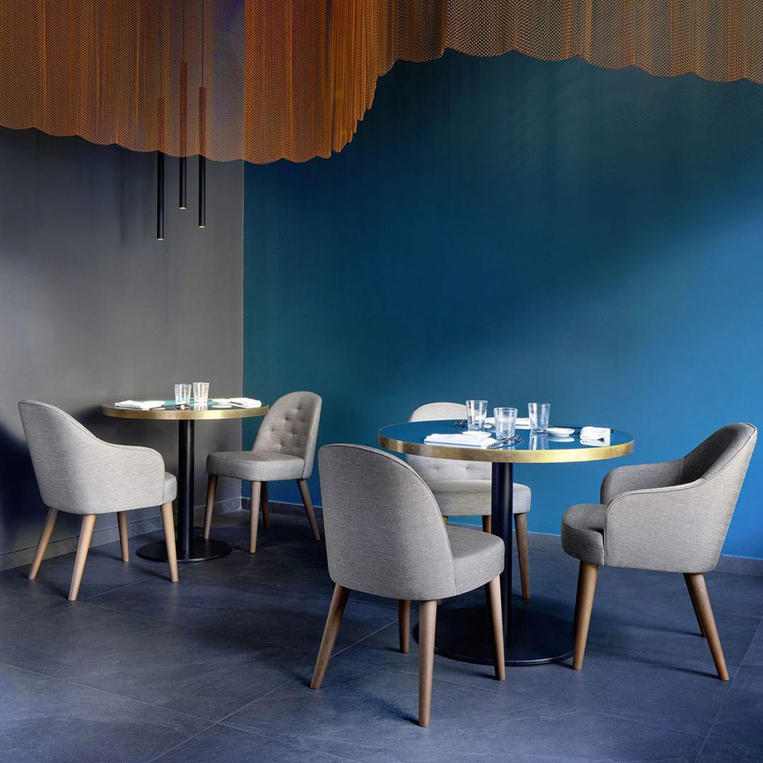 Gray upholstered chairs paired with a sleek round table, set against a deep blue wall and warm orange accents.
