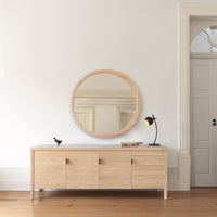Light oak sideboard with a smooth finish, paired with a round mirror and minimalistic black accents.