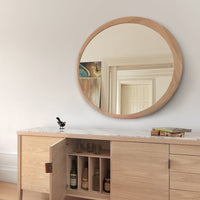 Round wooden mirror with a natural finish, reflecting soft beige and white hues from the room's decor.