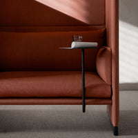 Rust-colored upholstered sofa with a sleek black side tray, featuring a minimalist design and shadow play on the surface.