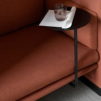 Modern black side table against rich, rust-colored sofa with a textured fabric. Elegant minimalist design.