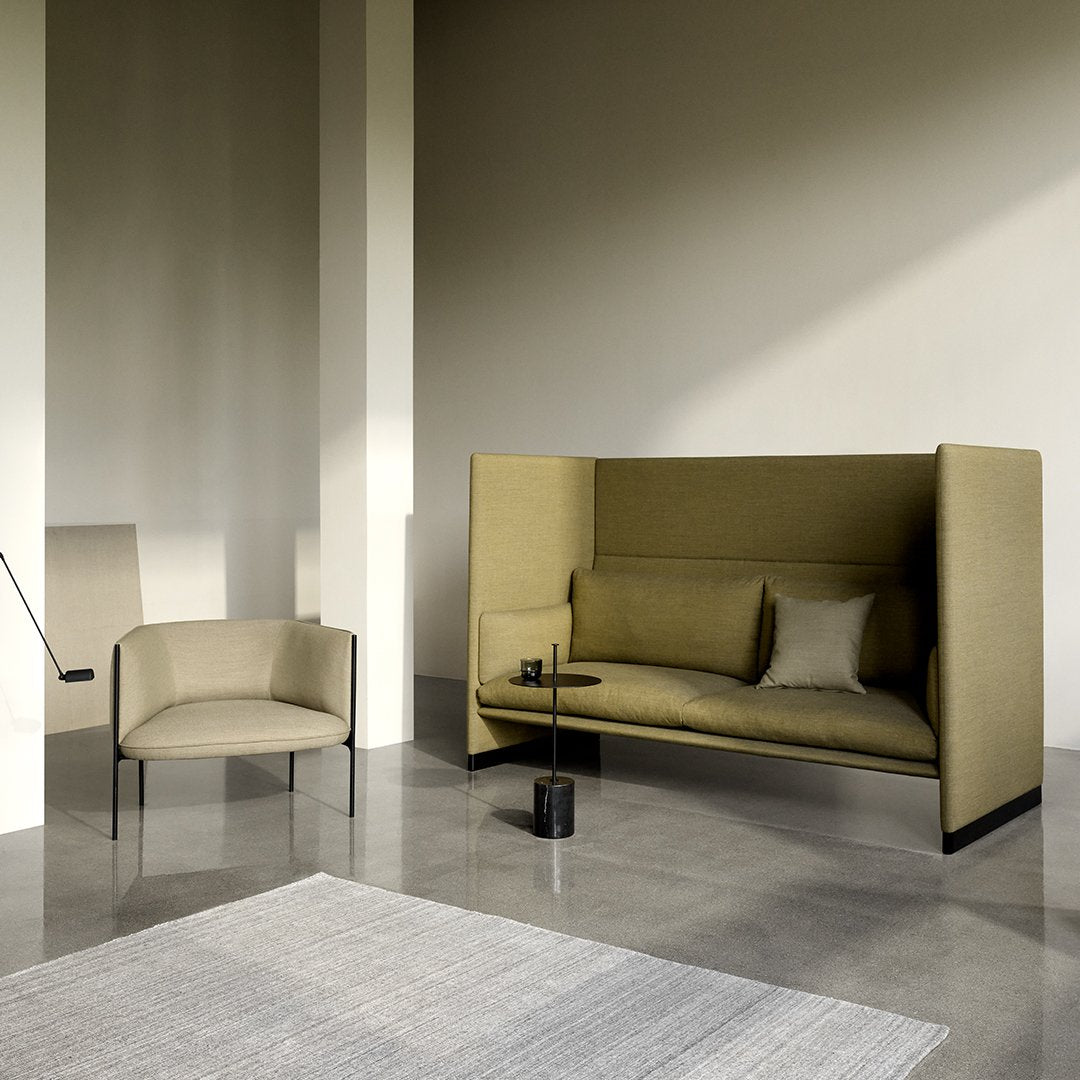 Olive green sofa with sleek black legs, paired with a light beige armchair in a minimalistic, modern setting.