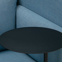 Sleek black round side table against a soft blue fabric sofa, creating a modern contrast.