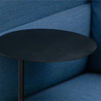 Black circular table on a blue fabric couch, showcasing a modern color contrast and sleek design.
