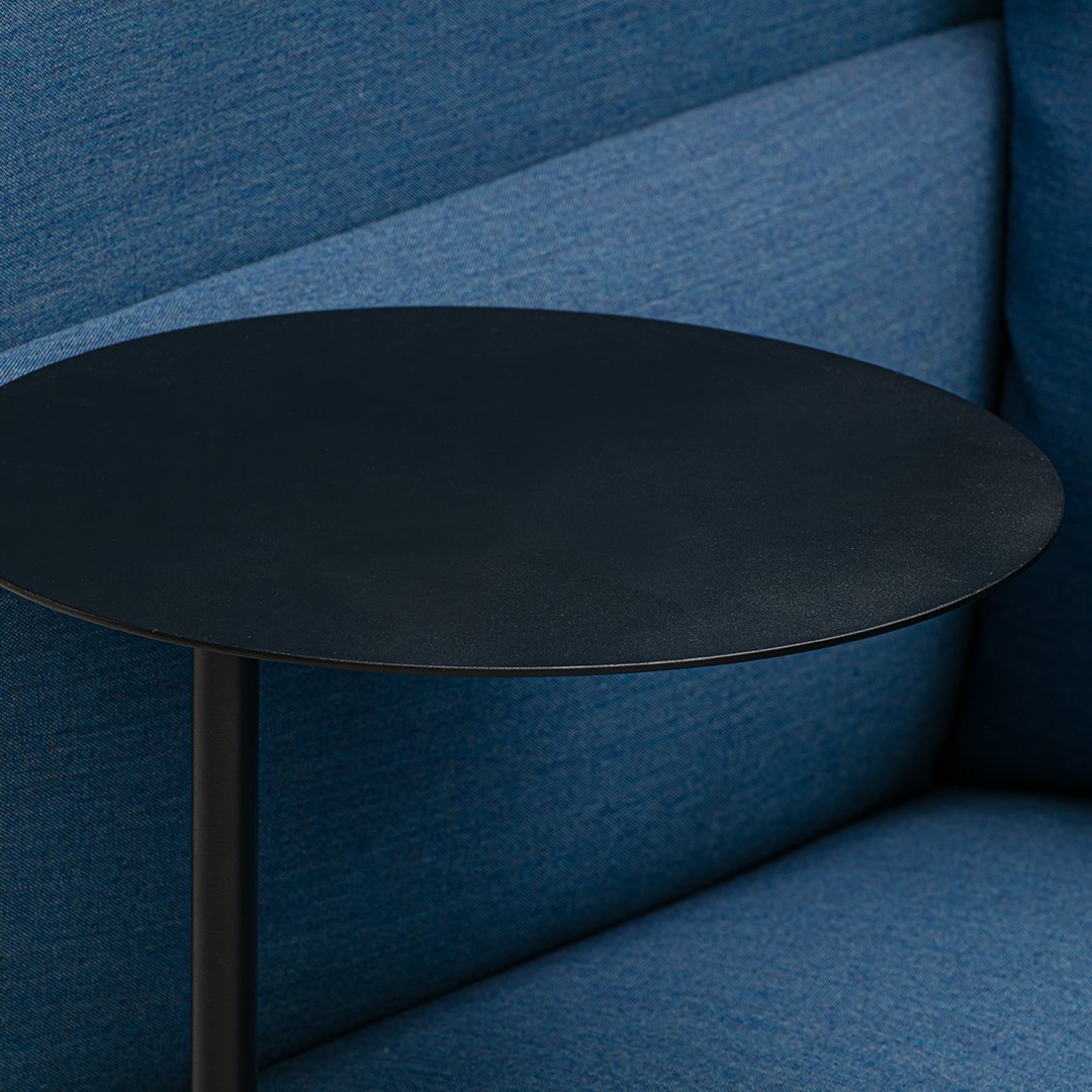 Black round table top contrasted against textured blue upholstery. Modern design with sleek colors and patterns.