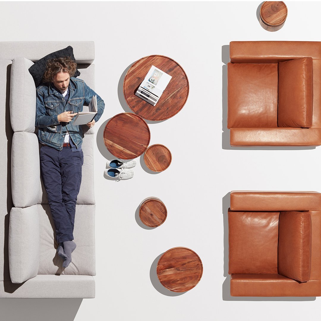 "Light gray sofa with brown leather armchairs and round wooden tables, featuring a modern minimalist design."