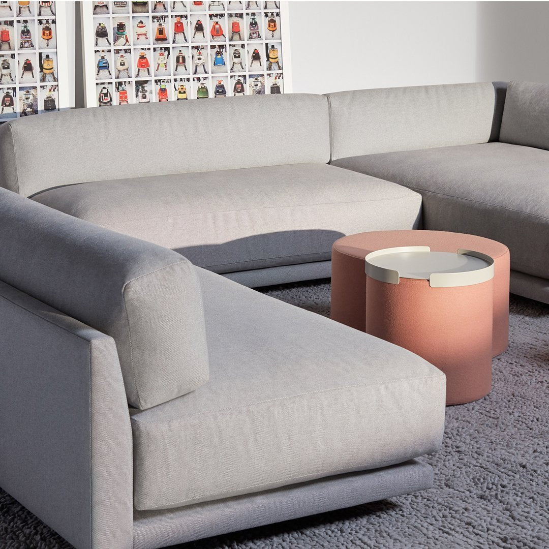 Light gray sectional sofa with smooth fabric and rounded edges, paired with a modern blush-colored coffee table.