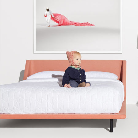 "Soft white bedding on a coral pink bed frame, featuring a textured quilted pattern and a minimalist design."