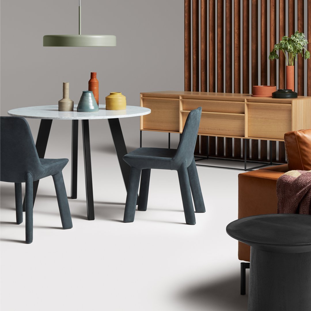 Modern dining set featuring a white round table, grey chairs, and wooden accents with earth-toned decor.