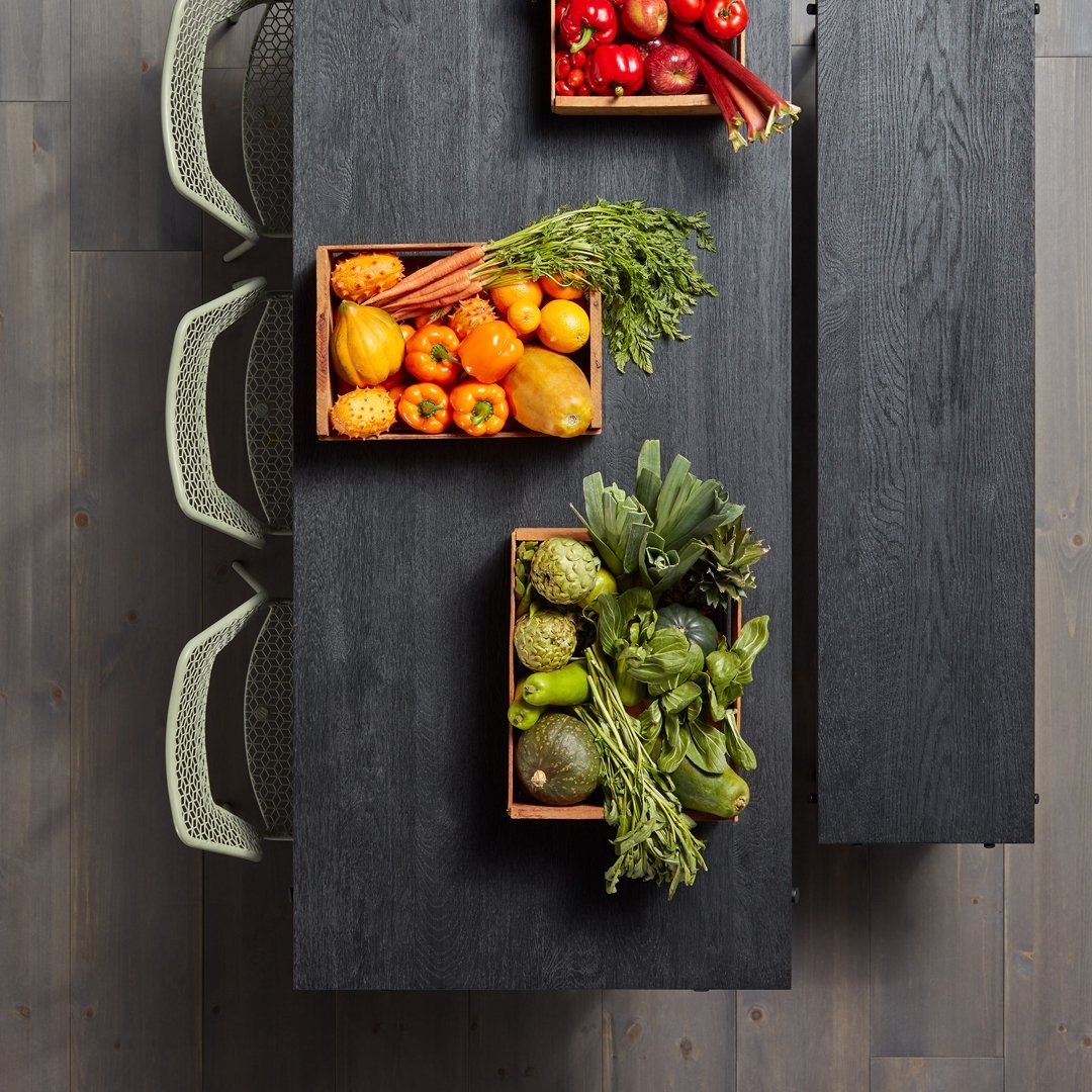 Vibrant assortment of orange, green, and red fruits and vegetables in wooden boxes atop a dark wooden table.