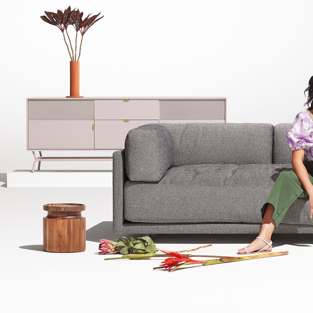 Gray textured sofa with green pants and a floral top, complemented by light wood and pink accents in a modern home setting.