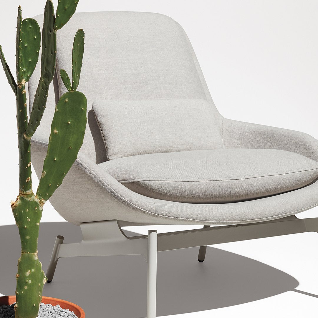 Light grey modern armchair with simple lines, complemented by a green cactus in a terracotta pot. Minimalist design focus.