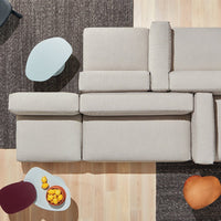 Light gray sectional sofa with modern design, paired with colorful accent tables on a dark patterned rug.