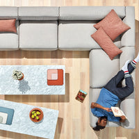 Gray sectional sofa with terracotta pillows, marble coffee table, and colorful patterned coasters on a light wood floor.