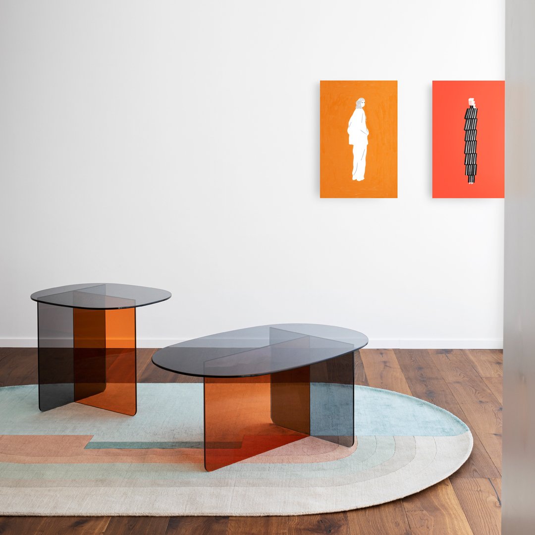 Two modern coffee tables with transparent black and amber hues, set against a light-colored area rug with muted pastels.
