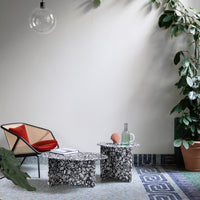 "Black and white floral patterned side tables on a textured blue and gray rug with green plant accents."