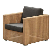 Natural woven rattan chair in light brown with a contrasting dark gray cushion. Modern, textured design for indoor/outdoor use.