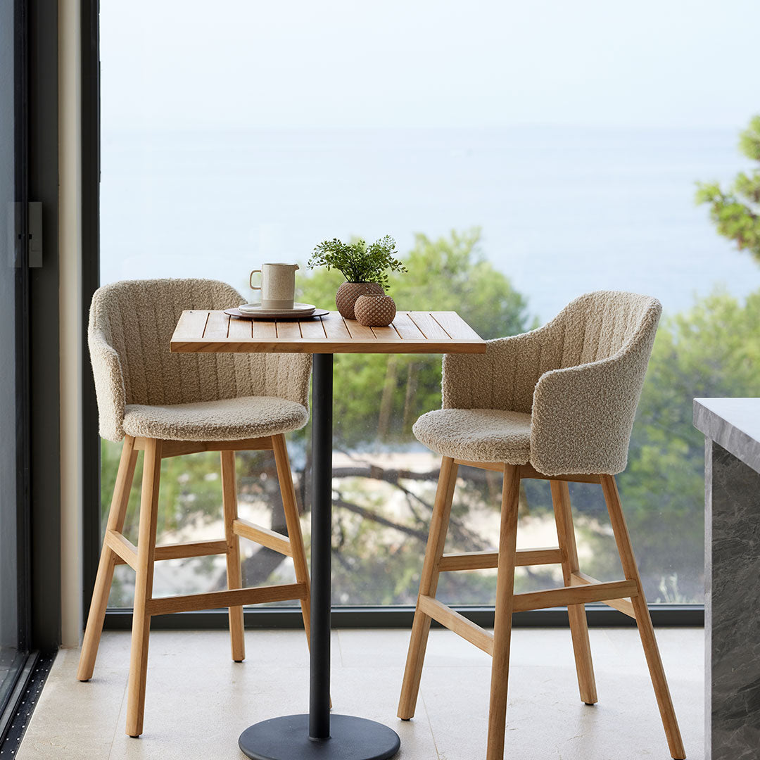 Neutral beige upholstered bar stools with light wooden legs, paired with a sleek, round black table.