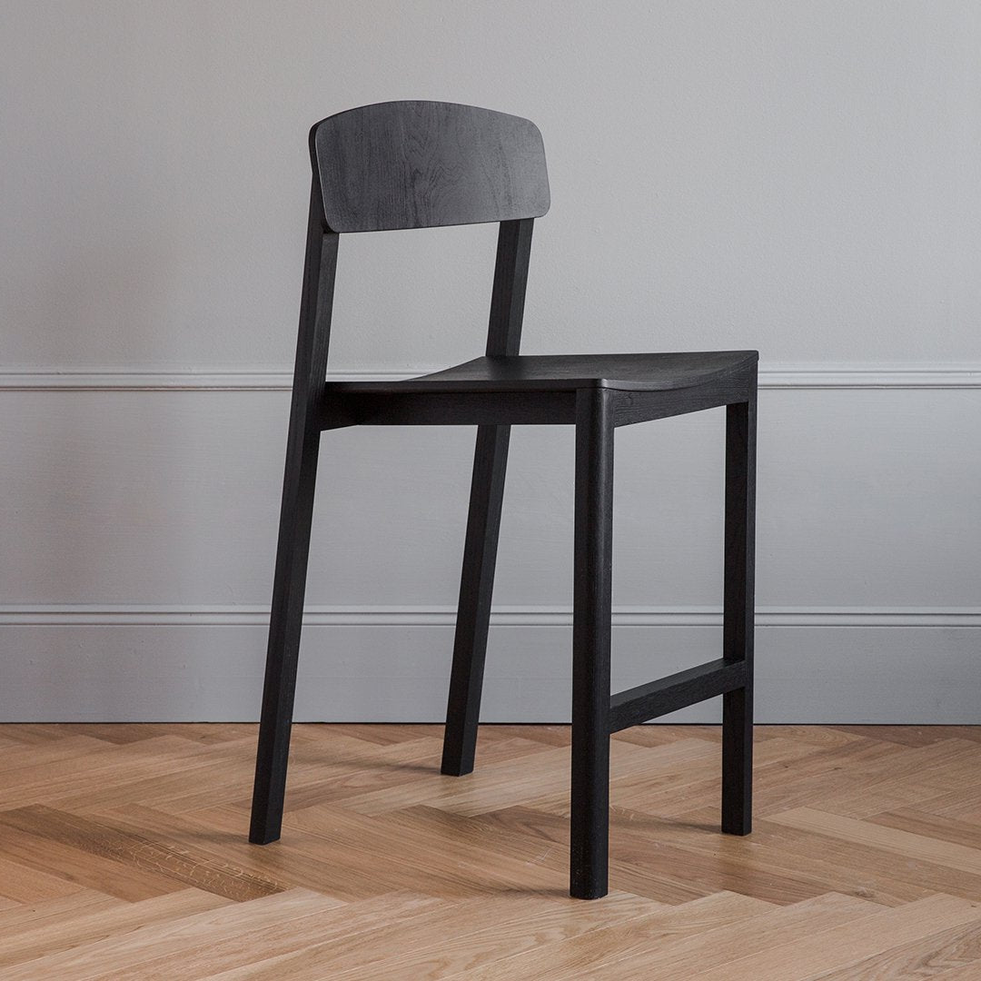 Sleek black wooden chair against a neutral wall, highlighting modern minimalist design and subtle texture.